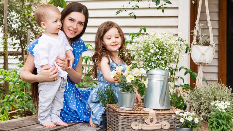 Deko-Trends für Garten, Terrasse und Balkon: Frau mit zwei Kindern in einem Garten beim Dekorieren