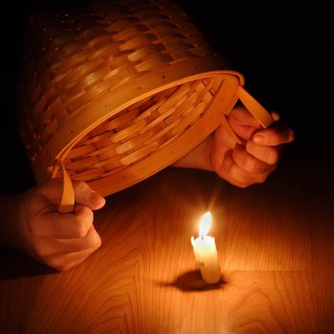 Hände halten Korb über Kerze: Warum sagt man: "Stell dein Licht nicht unter den Scheffel"? (Foto: IMAGO, IMAGO / YAY Images)